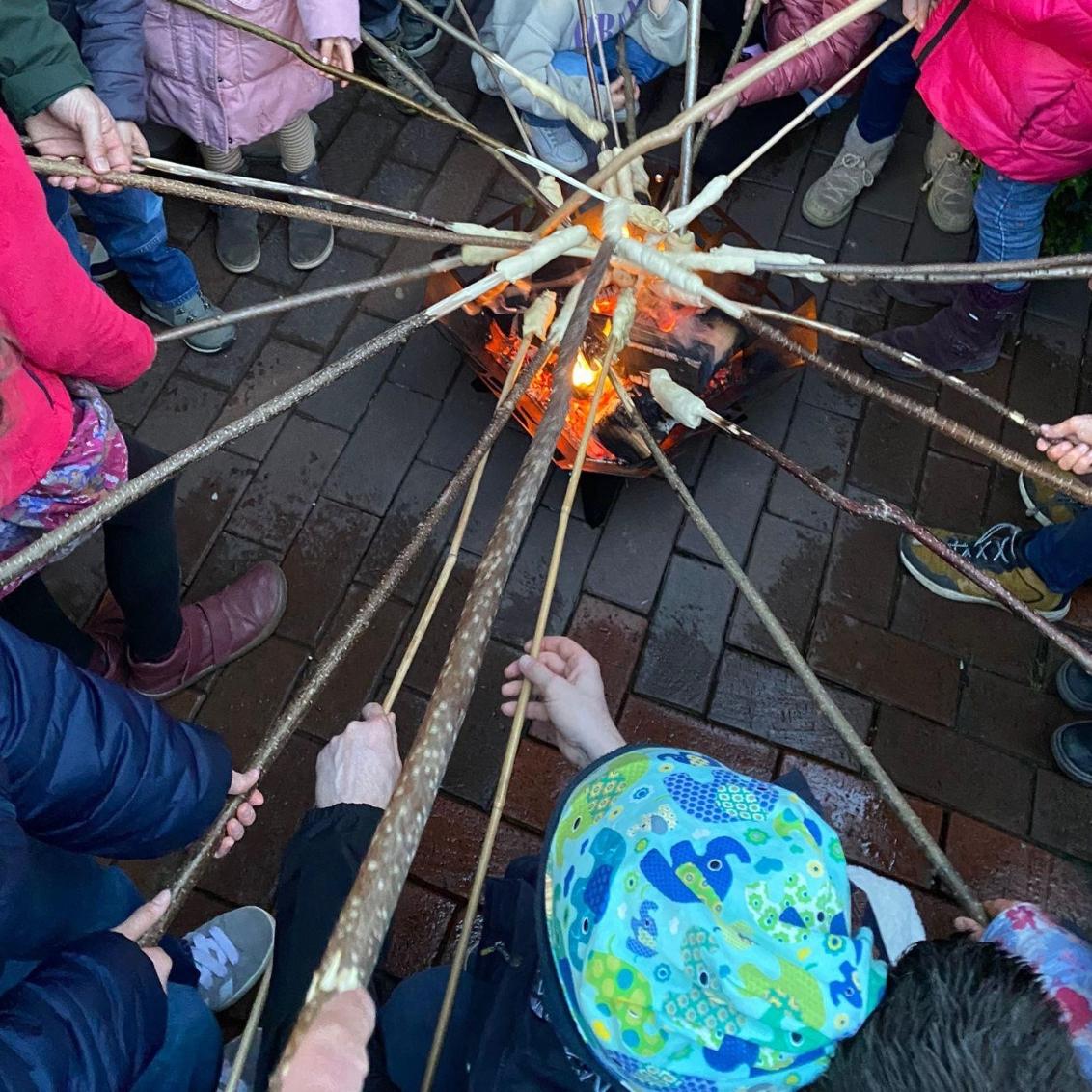 Kinder halten an Haselnussstöcken gewickelten Hefeteig über das glühende Feuer