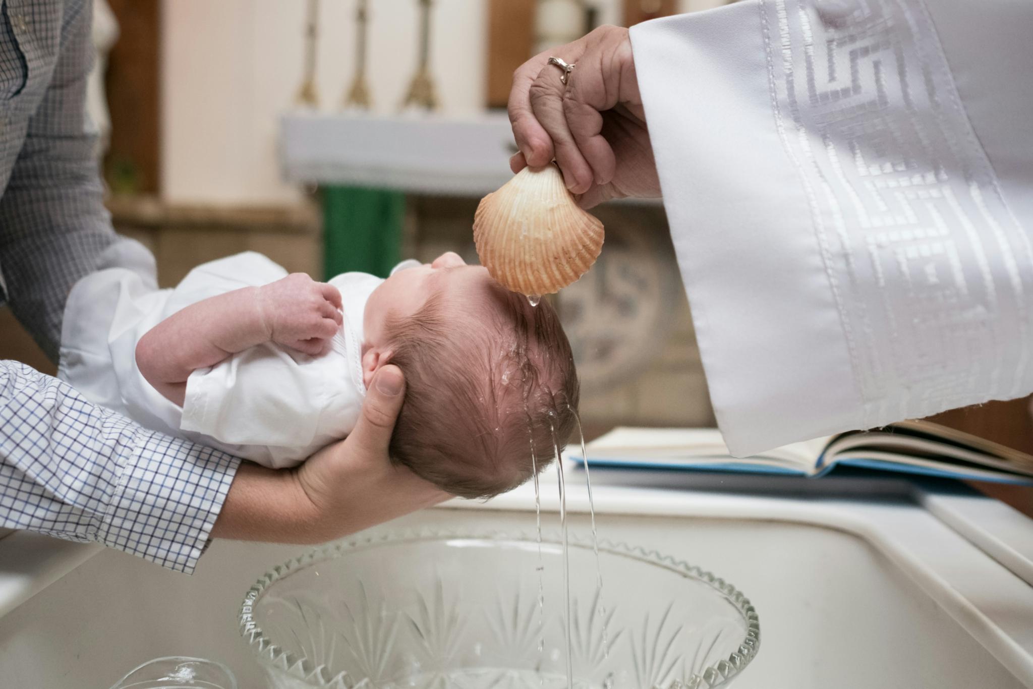 einem Säugling wird bei der Taufe Wasser über den Kopf gegossen