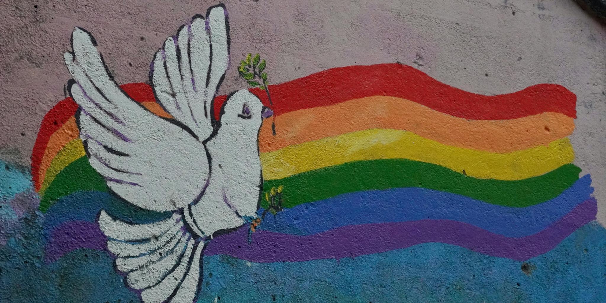 ein Regenbogen mit einer Friedenstaube auf eine Hauswand mit Kreide gemalt