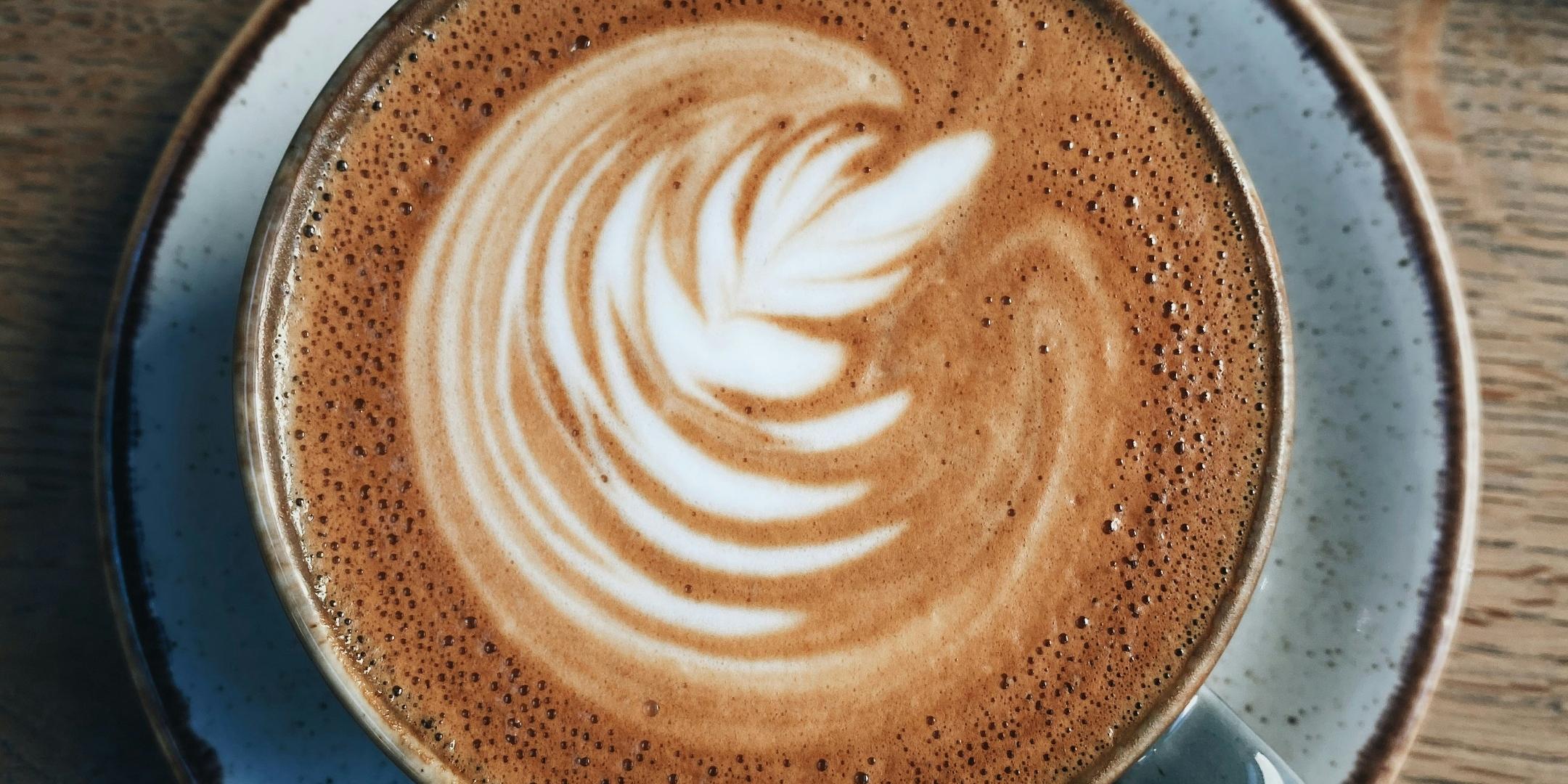 wir sehen in eine Tasse mit Cremigen Kaffee, im Milchschaum ist ein Blatt sichtbar